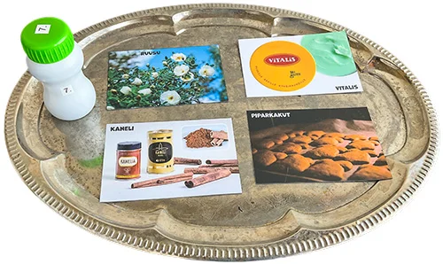 Nenäpeli käytössä: tuoksupullo ja 4 kuvaa eri tuoksuista: ruusu, kaneli, Vitalis ja piparkakut.